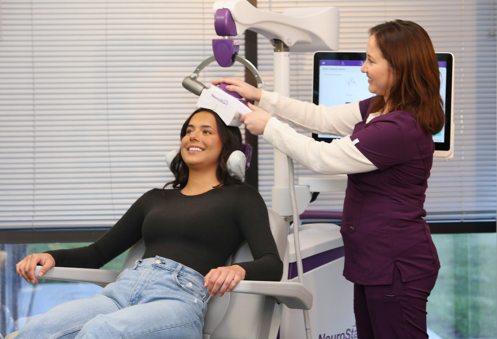 Clinician positioning a NeuroStar® coil on a smiling seated patient